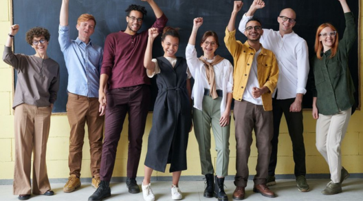 Questa immagine mostra un gruppo entusiasta di persone sui trent'anni in piedi davanti a una lavagna, che alzano le braccia con gioia