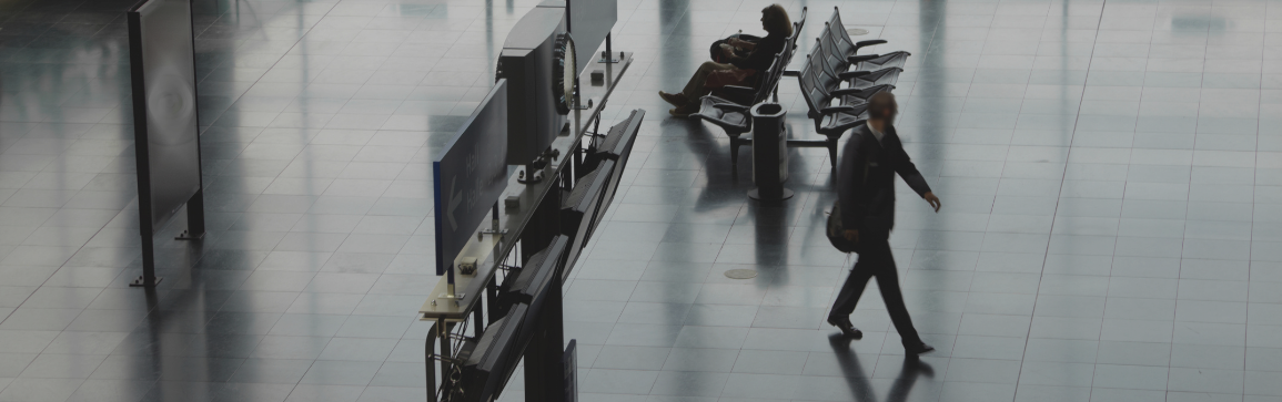 Immagine di un gate di un aeroporto con una persona che cammina e un'altra seduta nella sala d'attesa