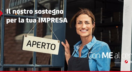 Donna sorridente davanti a porta di negozio con scritto “Aperto”. In alto a sinistra scritta “Il nostro sostegno per la tua impresa”, in basso a destra scritta “Con Me al centro” e logo Unicredit.